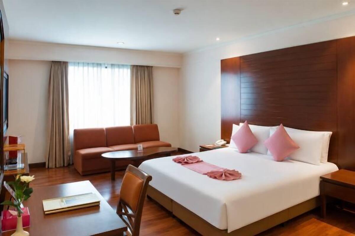 A hotel room with a bed, a sofa, a small table, a TV, and a window with curtains.