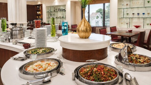 Een buffetopstelling met verschillende stations voor eten, een decoratieve vaas in het midden en een glazen displaykast in een hotelrestaurant.