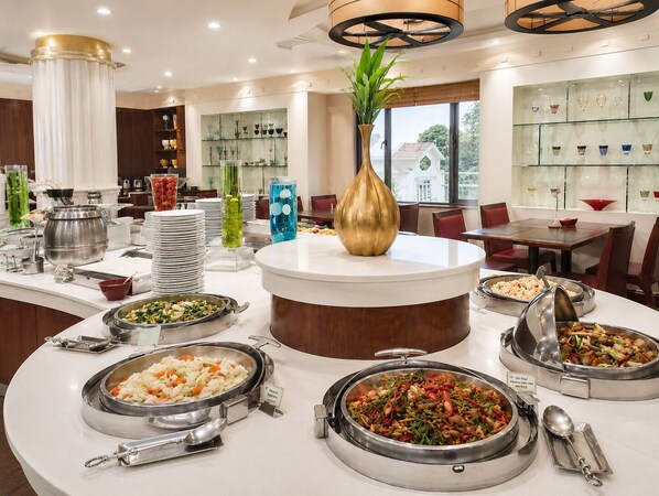 A buffet setup with various food stations, a central decorative vase, and a glass display case in a hotel dining area. - The Palazzo Hotel (Bangkok)