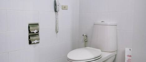A white toilet with a footrest, a paper towel dispenser, and a hand dryer.