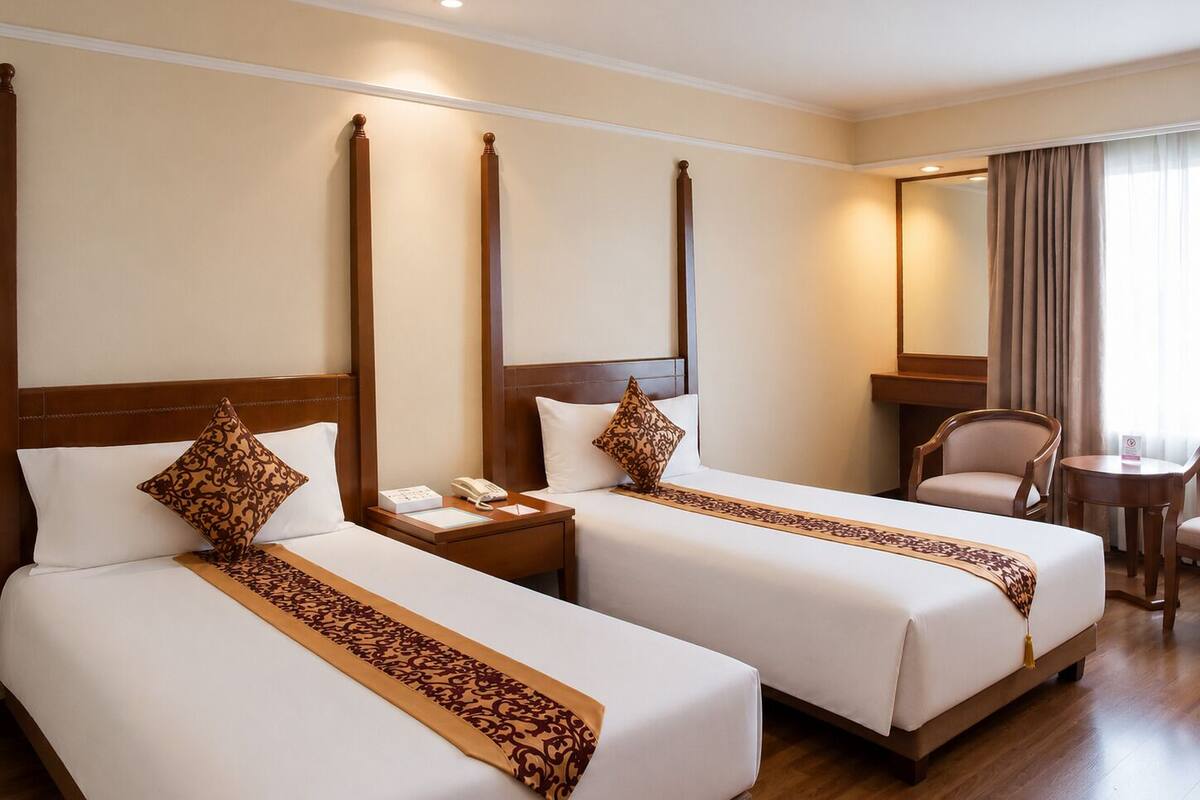 A hotel room with two beds, a bedside table with a phone, a chair, and a small table.