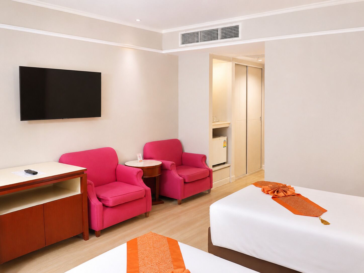 Habitación de hotel con dos camas, un televisor, un escritorio y dos sillones rosados.