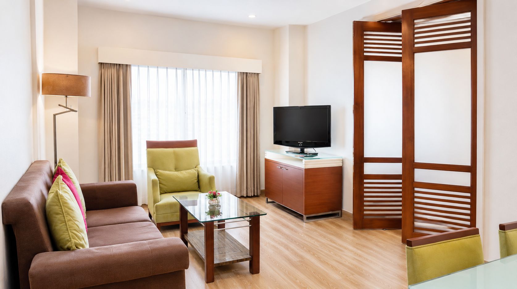 A hotel room with a sofa, armchair, television, and a wooden partition.