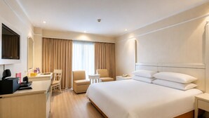 Een hotelkamer met een bed, twee stoelen, een bureau, een televisie en een telefoon.