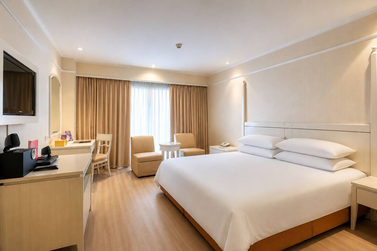 A hotel room with a bed, two chairs, a desk, a TV, and a phone.