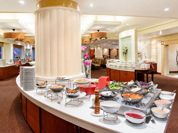 A buffet setup with various food stations, a large column, and a dining area in the background. - The Palazzo Hotel (Bangkok)