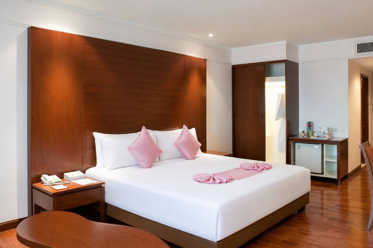 A hotel room with a large bed, bedside tables, a desk with a chair, and a small kitchenette.
