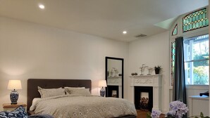 Une chambre à coucher avec un lit, des tables de chevet, une cheminée et une fenêtre avec des rideaux.