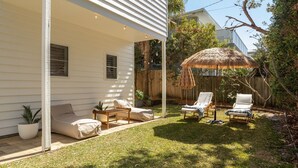 Une terrasse couverte avec des sièges d’extérieur, un parasol en chaume et une clôture en bois en arrière-plan.