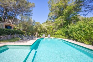 Une piscine entourée de chaises longues, bordée d’arbres et d’un bâtiment dont la porte est bleue.