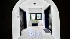 A hallway with a white tiled floor, a black door on the left, a black door on the right, and a window at the end. - Luxury, contemporary 4-Bed Apartment in Ikoyi (Lagos)