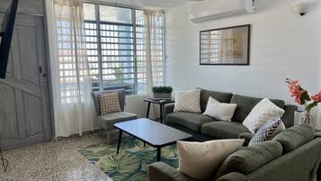 A living room with a grey sofa, a small table, a chair, and a window with curtains.
