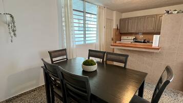 A dining area with a table and chairs, a window with curtains, and a kitchen area with cabinets and appliances.