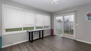 Una habitación con ventanas amplias, una puerta corrediza de vidrio a un patio y una lámpara en el techo.