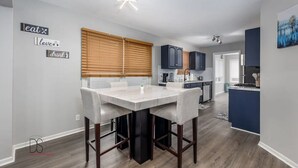 Una cocina moderna con una isla central, persianas de madera y una zona de comedor con una mesa y sillas de mármol.