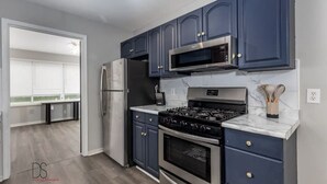 Una cocina moderna con armarios azul oscuro, un refrigerador de acero inoxidable, un microondas, una estufa a gas y un horno empotrado.