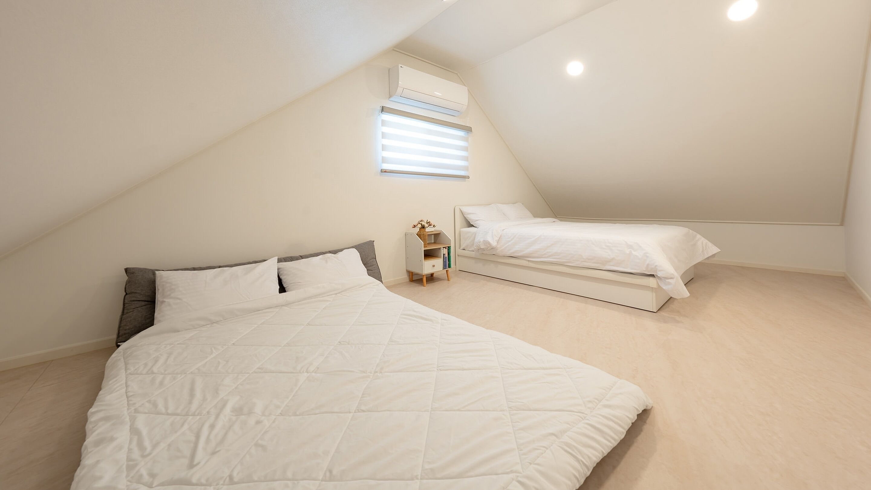 A bedroom with a large bed, a smaller bed, and a window with blinds.