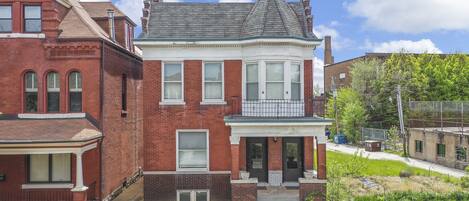 A two-story brick house with a bay window, a front porch, and a small front yard.