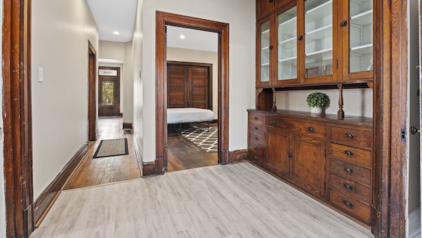 A hallway with wooden cabinets, a mirror, and a bed in the background.