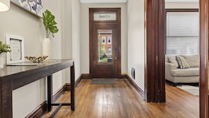 A wooden hallway with a door labeled "Entrance," a framed certificate on a table, and a plant.