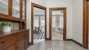 A hallway with a wooden cabinet, a potted plant, and a checkered floor leading to a dining area with a ceiling fan.