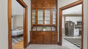 A wooden cabinet with multiple drawers and glass doors, leading to a bedroom with a bed and a patterned rug.