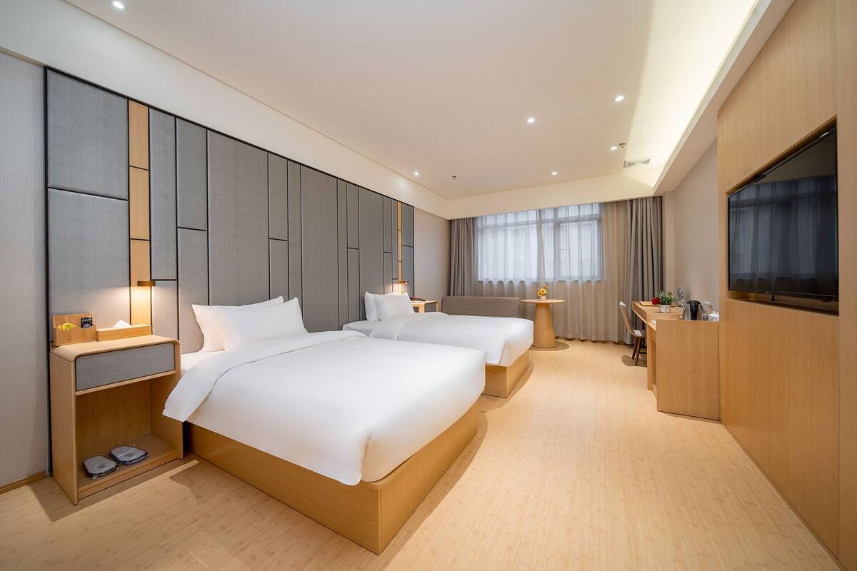 A modern hotel room with two beds, a desk, a TV, and a minibar.