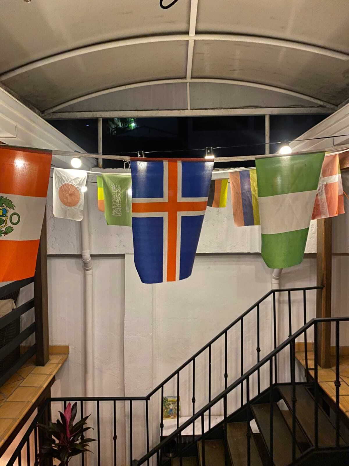 Una escalera con barandilla, una pared con ventana y banderas colgadas del techo.