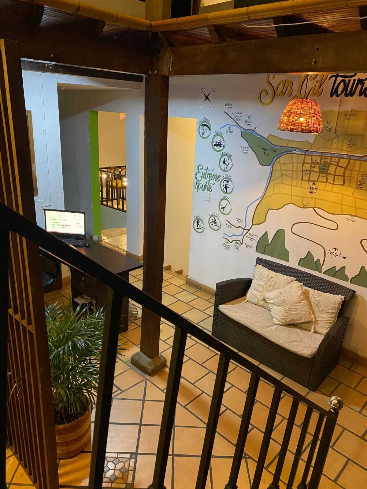 A hotel lobby with a map highlighting extreme sports activities, a seating area with a cushioned bench, and a staircase leading to an upper level.