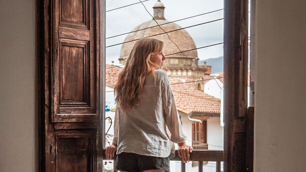 Une personne se tient sur un balcon, d’où l’on peut admirer un bâtiment surmonté d’un dôme.