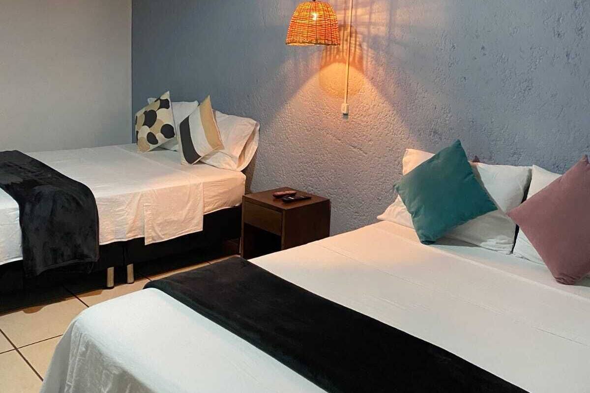 A bedroom with two beds, a hanging lamp, and a nightstand.
