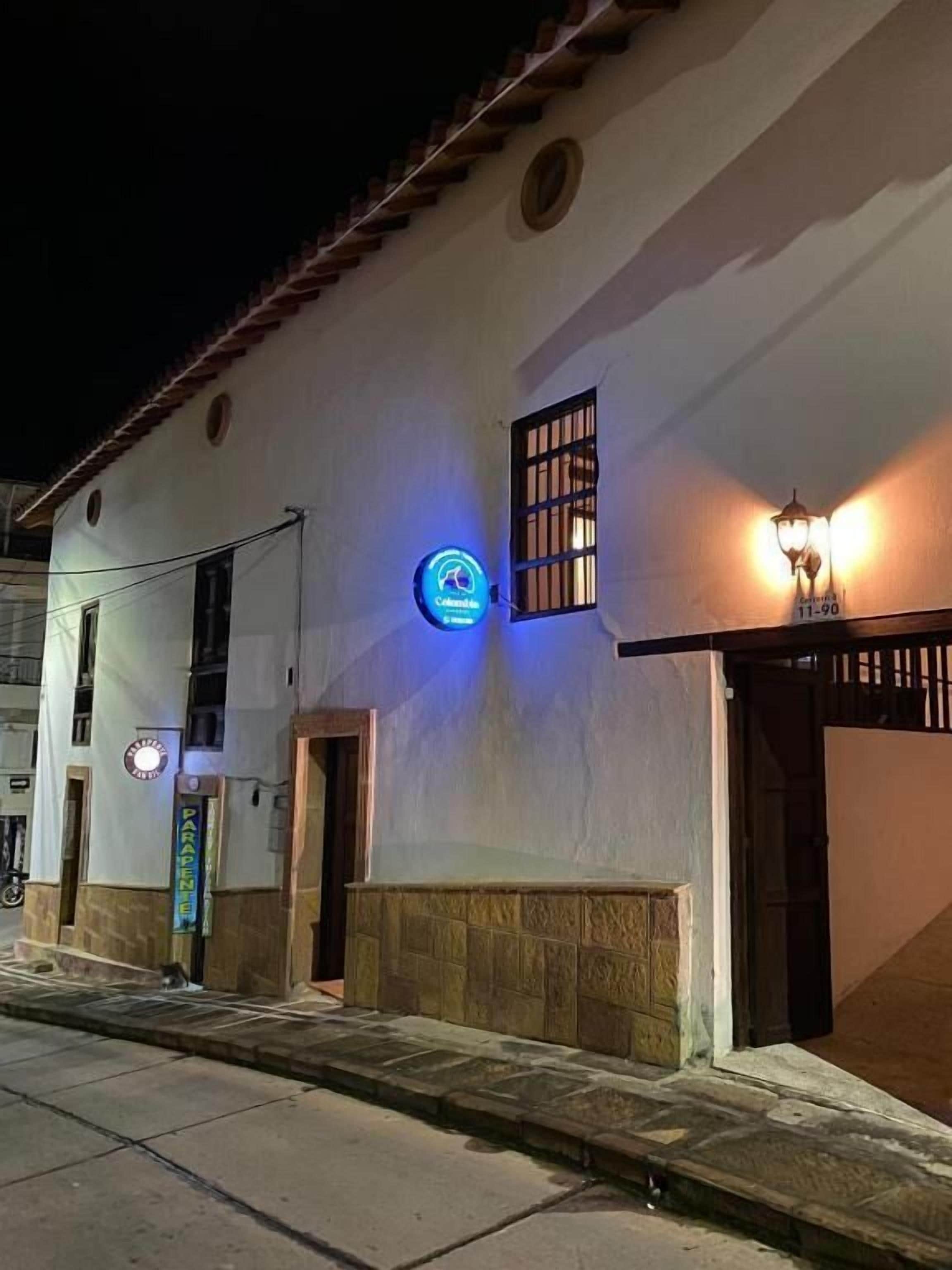 Un bâtiment blanc avec un toit recouvert de tuiles, une enseigne lumineuse et un lampadaire.