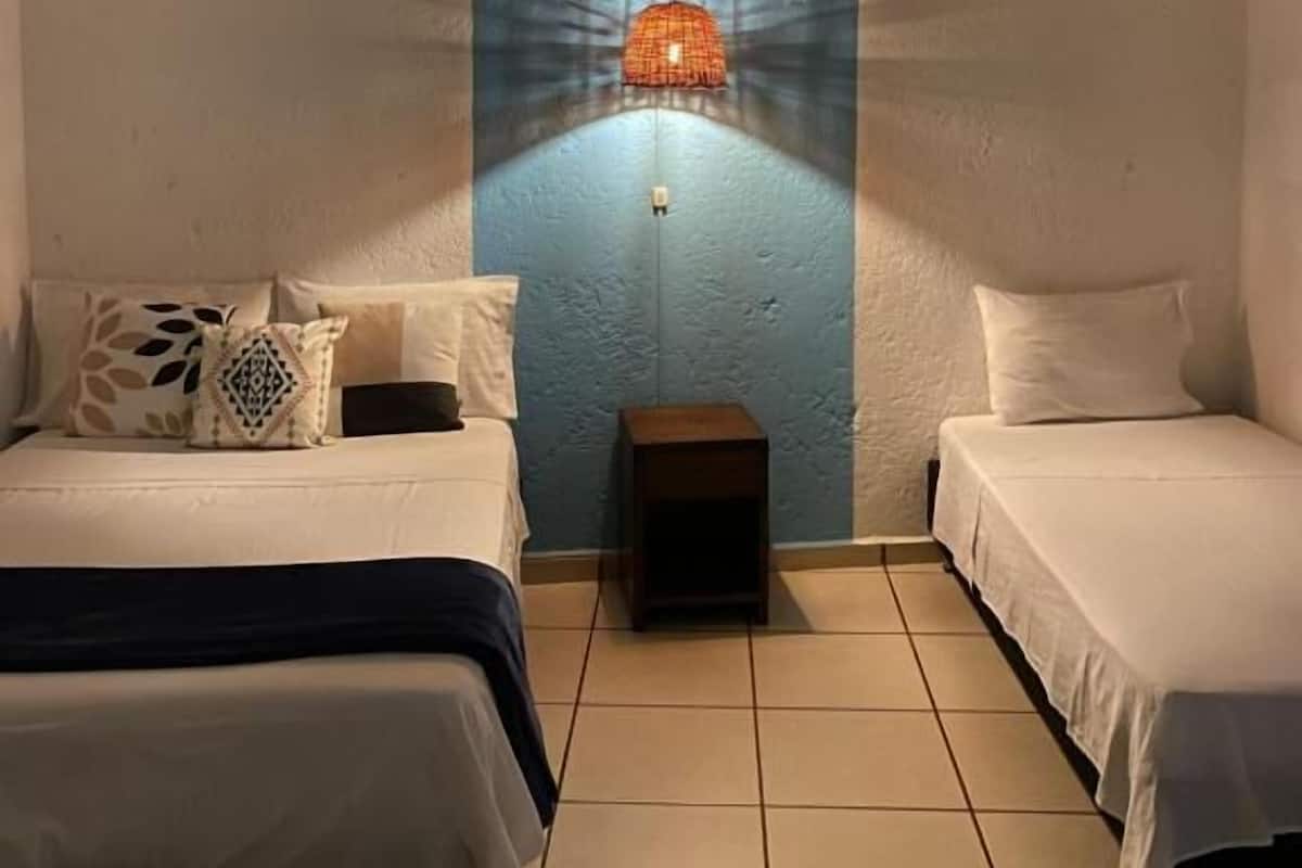 A room with two beds, a small table, and a hanging light fixture.