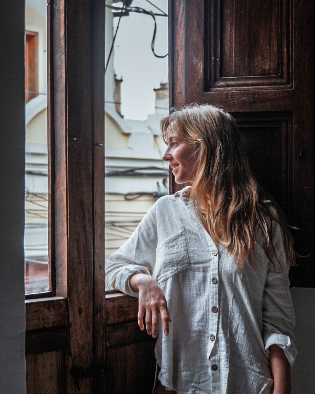 A person leaning on a wooden door with a window, looking outside.