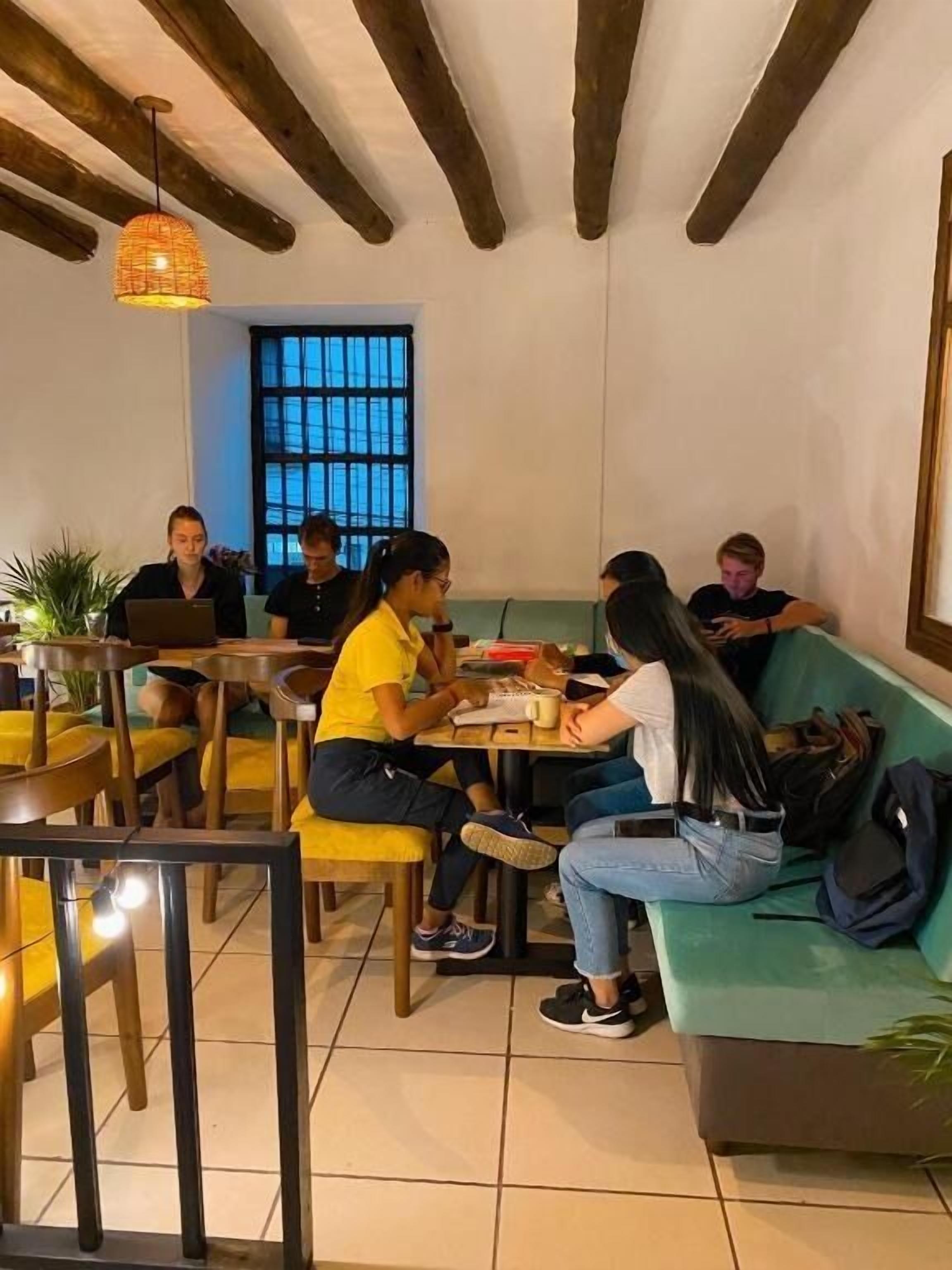 A group of people sitting at tables in a cafe with wooden furniture and a hanging light fixture.