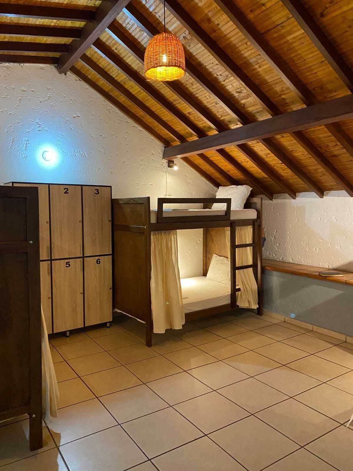 A dormitory room with bunk beds, a wooden wardrobe, and a hanging light fixture.