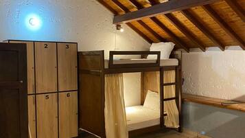 A dormitory room with bunk beds, a wooden wardrobe, and a hanging light fixture.