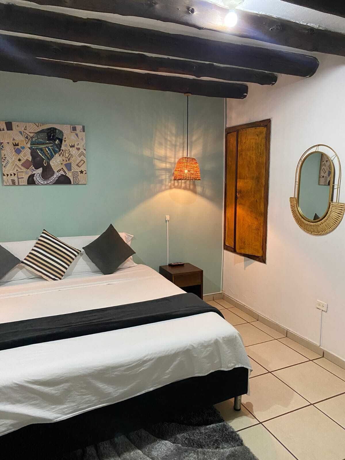 A bedroom with a bed, a nightstand, a wall-mounted mirror, and a painting.