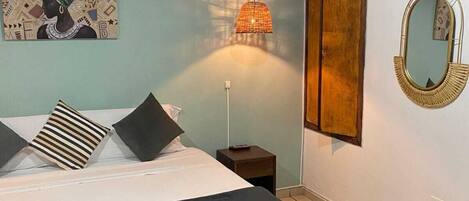 A bedroom with a bed, a nightstand, a wall-mounted mirror, and a painting.