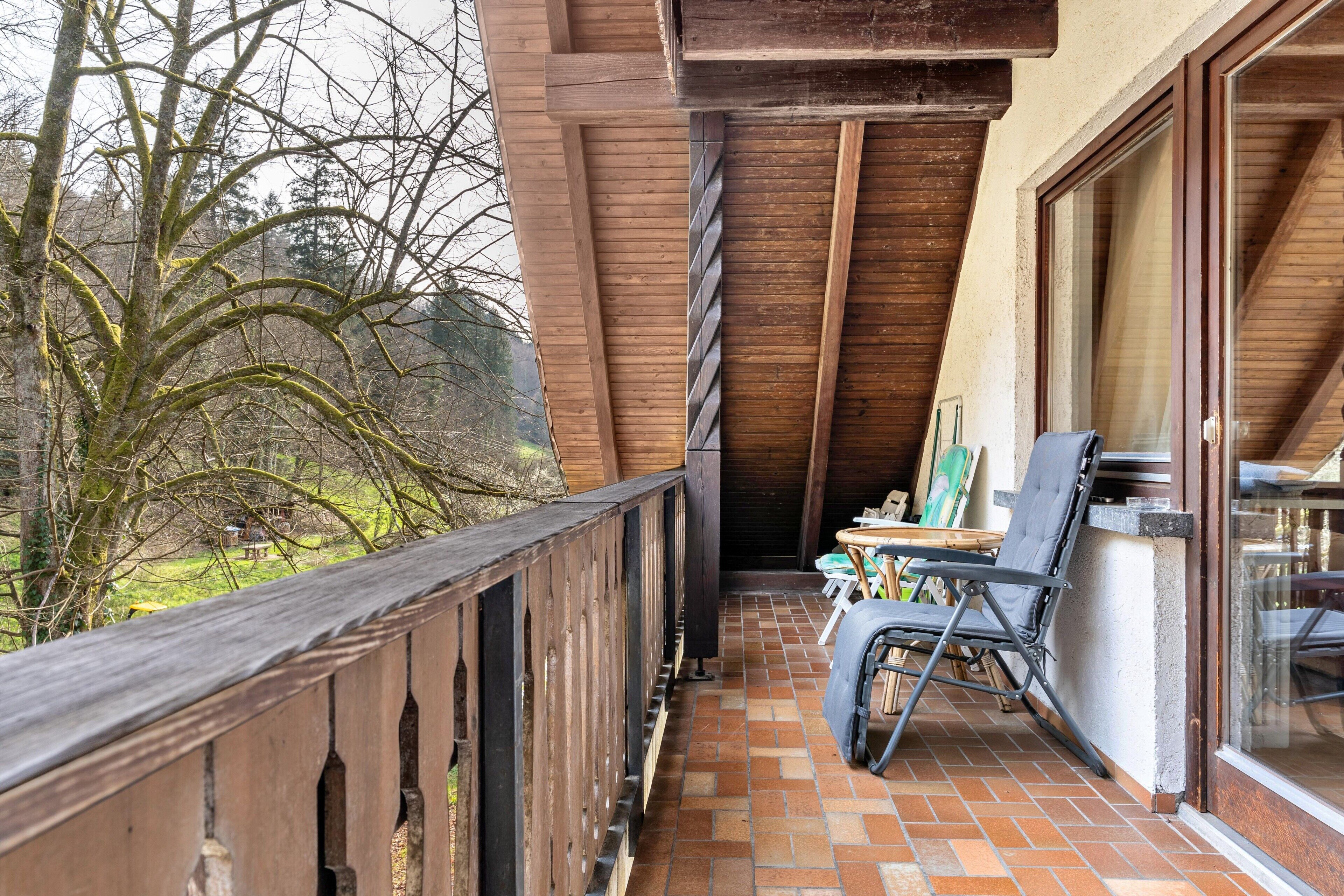 A wooden balcony with a tiled floor, a chair, and a table.