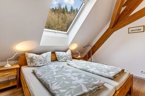 A bedroom with a skylight, wooden beams, a bed with floral bedding, bedside lamps, and a framed picture on the wall.