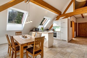 A modern kitchen with skylights, wooden beams, a dining area with a table and chairs, and a view of trees outside.
