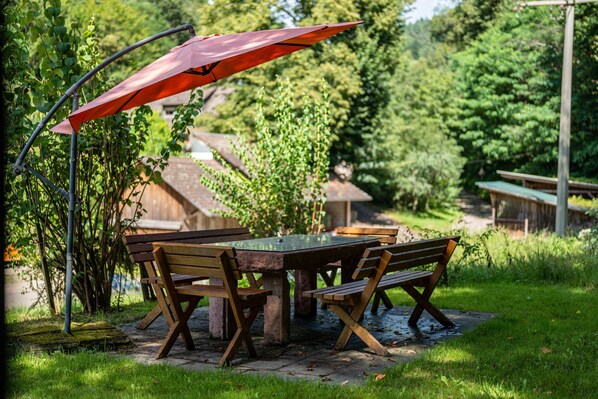 A wooden table with benches, an umbrella, and a garden setting.