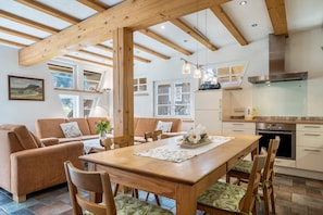 Una cocina moderna con vigas de madera, un comedor con mesa y sillas de madera, y una sala de estar acogedora con un sofá.
