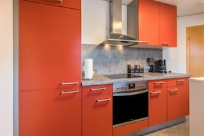 Une cuisine moderne avec des meubles de couleur rouge, une hotte de cuisson en acier inoxydable et un four encastré.