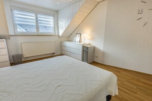 Une chambre à coucher avec un grand lit, une commode, un radiateur, une fenêtre avec des stores et un plafond en pente.