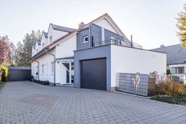 Une maison moderne à deux étages, dotée d’un garage, d’une allée couverte et d’un petit jardin.