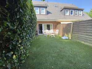 A residential backyard with a lawn, a wooden fence, and a patio area with outdoor furniture.