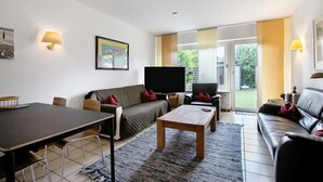 Ein Wohnzimmer mit Sofa, Couchtisch, Fernseher und Esstisch.