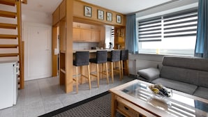 A compact living space with a kitchenette, a sofa, a coffee table, and a window with blinds.